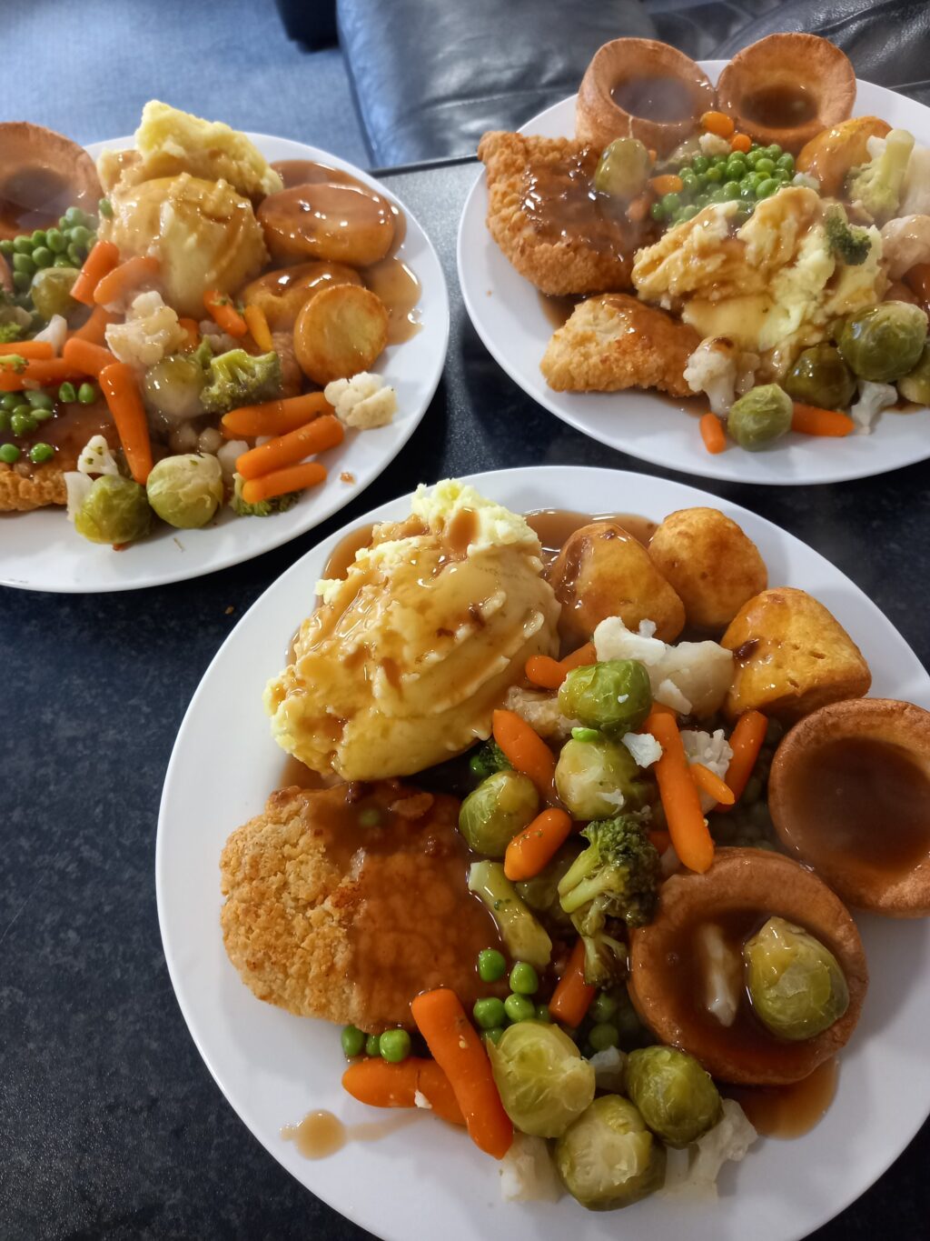 Three plates of a delicious roast dinner, including yorkshire pudding, potato, vegetables and gravy.