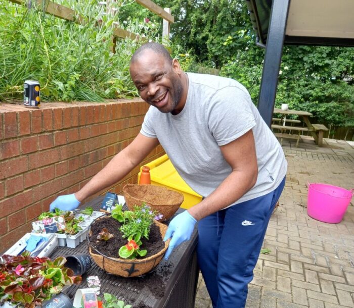 A man is wearing gloves and stood next to some plants and pots. He has a big smile on his face.