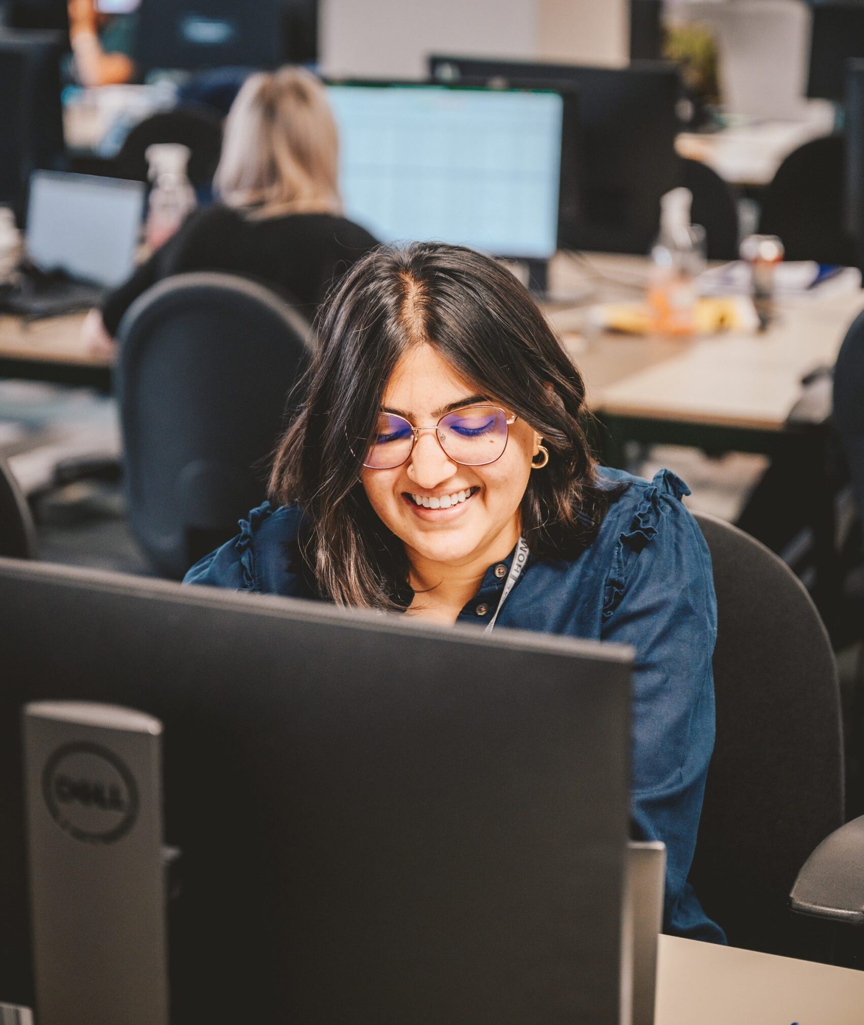 Anokhee, sat smiling at a desk in front of a computer.