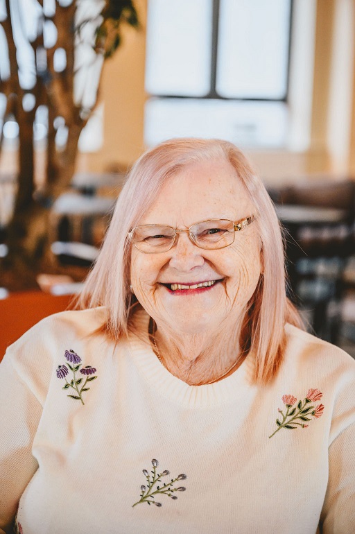 A photo of Pam. She's wearing a pink floral top and smiling at the camera.