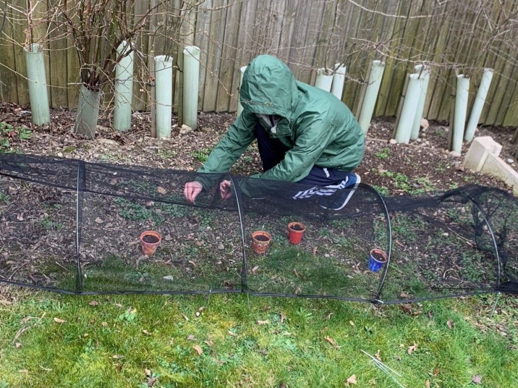 A customer knelt down gardening. They are wearing a waterproof coat with the hood up.